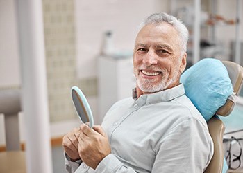 man smiling while holding dental mirror